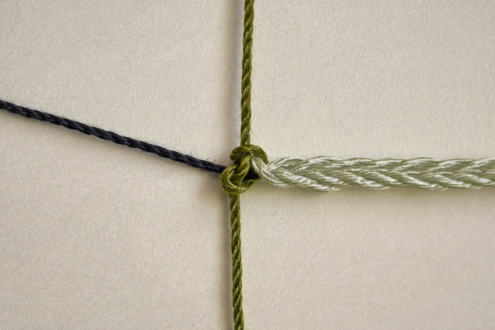 Três fios de cores diferentes unidos num único nó, seguindo como um cordão só